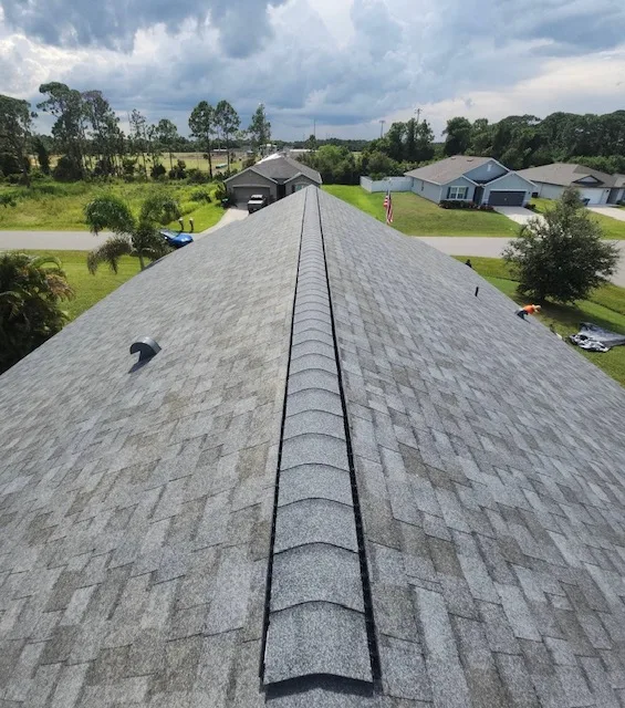 Roof of a residential home in Palm Bay, showcasing new gray asphalt shingles, with a clear view of the ridge and surrounding landscape, emphasizing quality roofing and restoration services by American Masters Roofing.